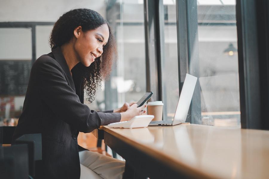 A young woman working on her laptop while holding a phone.